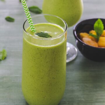 Mango green smoothie in a glass with straw and mint leaf garnish