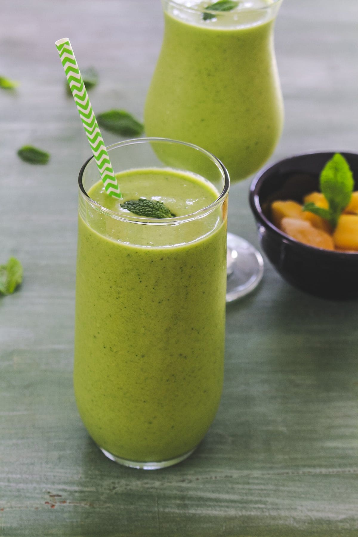 Mango green smoothie in a glass with straw and mint leaf garnish