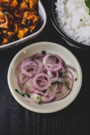 Onion salad in a plate with side of paneer curry and rice