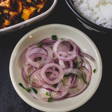 Onion salad in a plate with side of paneer curry and rice