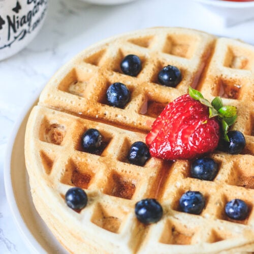 Close up shot of eggless waffles with toppings of berries and maple syrup