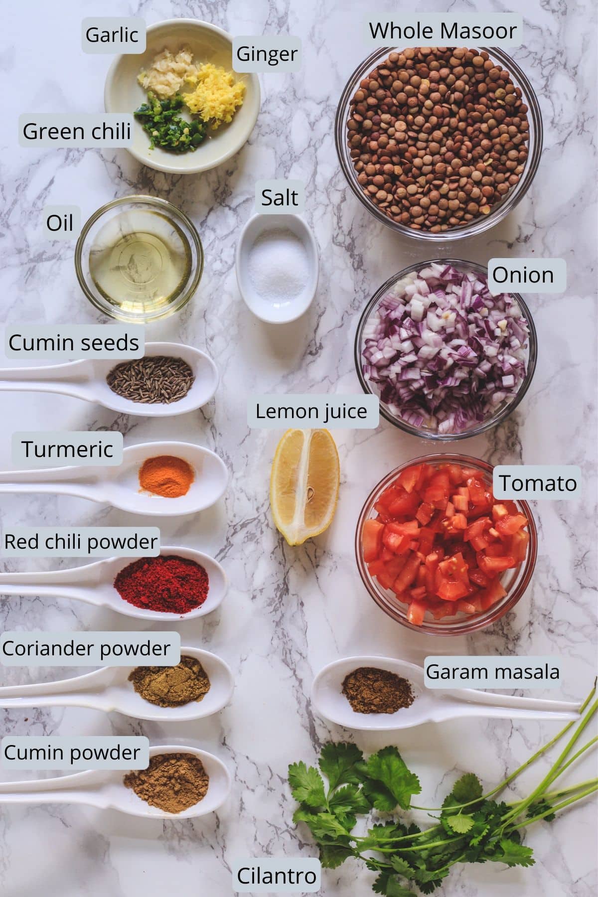 Whole masoor dal recipe ingredients laid down on marble surface