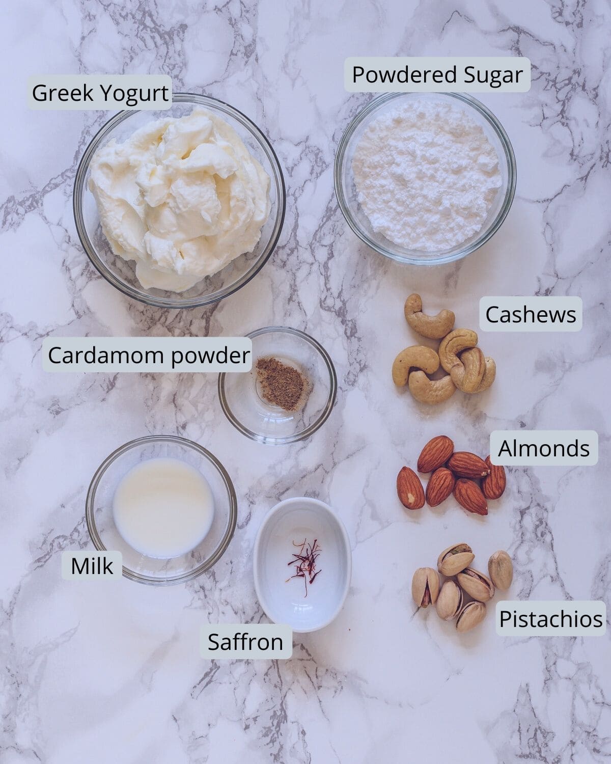 image of ingredients used in shrikhand recipe. Showing greek yogurt, powdered sugar, nuts, milk, saffron, cardamom powder