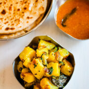 Top view of batata bhaji in a bowl with side of puran poli, katachi amti and rice.