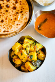 Top view of batata bhaji in a bowl with side of puran poli, katachi amti and rice.