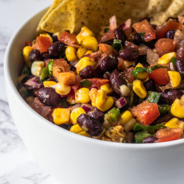 black bean and corn salsa in a white bowl with few tortilla chips on side