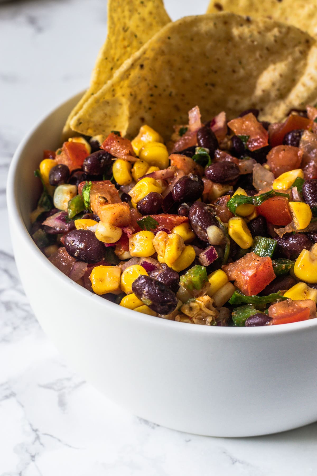 Black bean and corn salsa in a white bowl with few tortilla chips on side