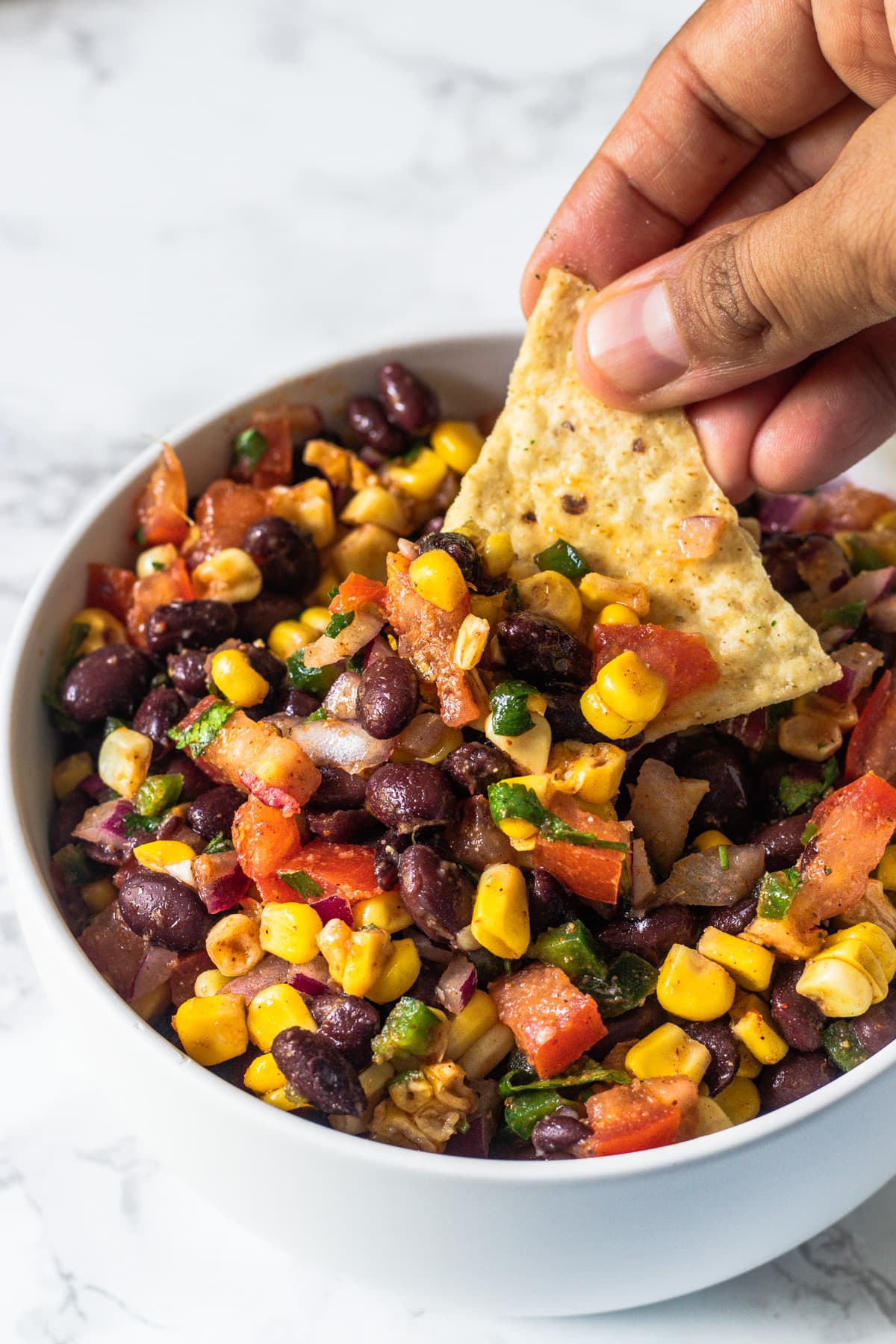 Taking a scoop of black bean and corn salsa using tortilla chip.