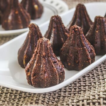 Image of chocolate modak arranged on a white plate with few modak in another plate place on the back side.