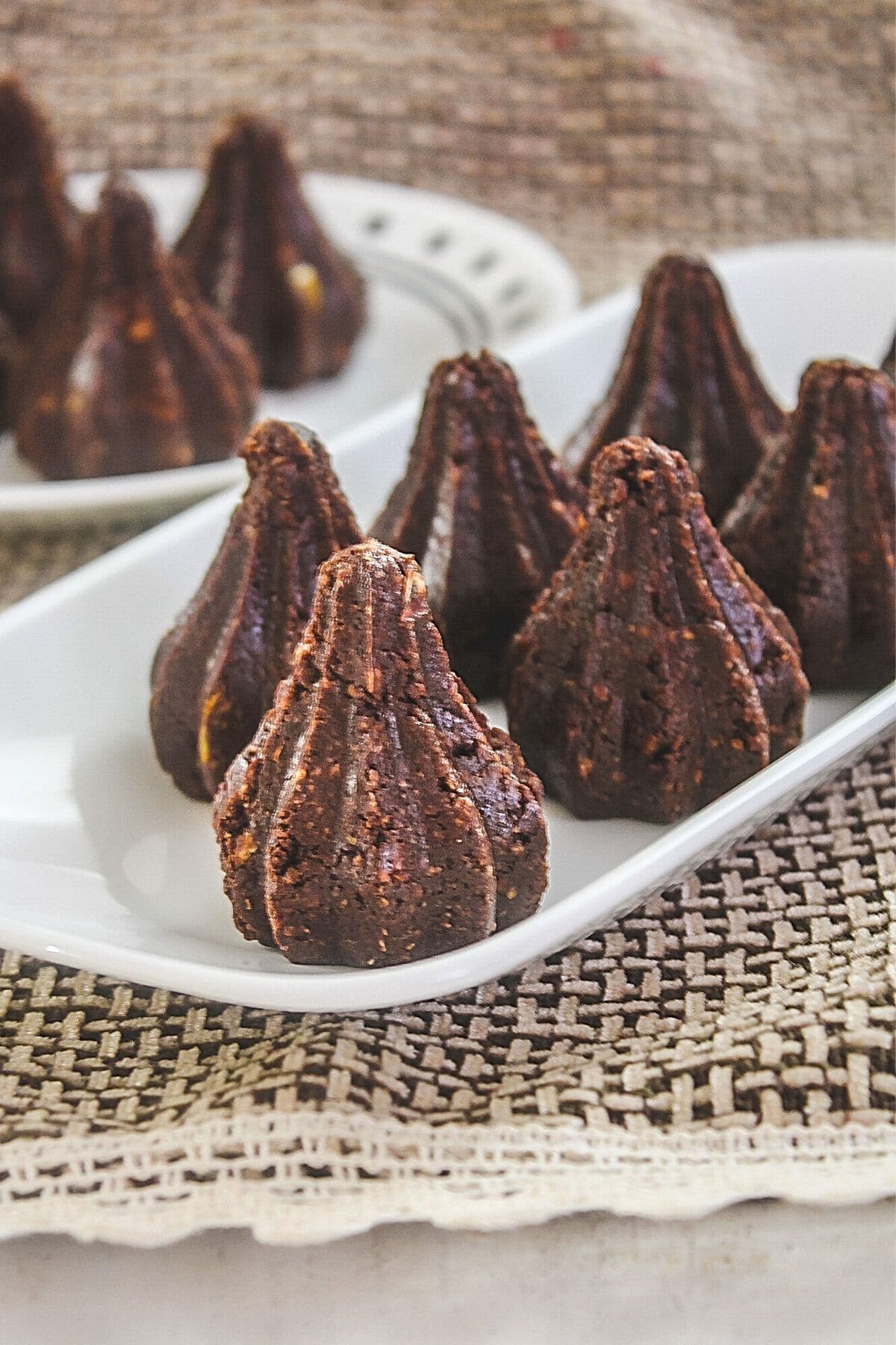 Image of chocolate modak arranged on a white plate with few modak in another plate place on the back side.