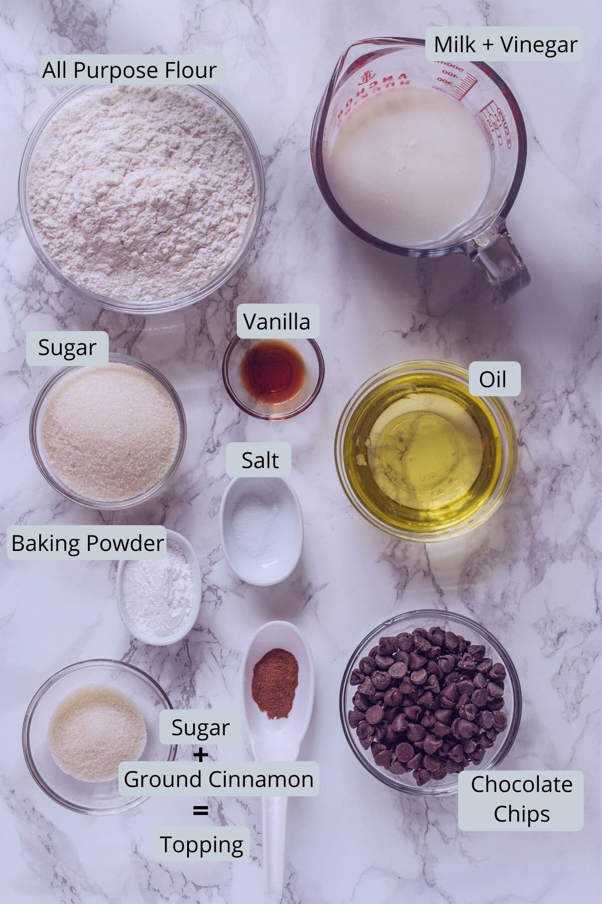 Image of ingredients used in eggless chocolate chip muffins. Includes milk, vinegar, oil, vanilla, flour, sugar, baking powder, salt, chocolate chips