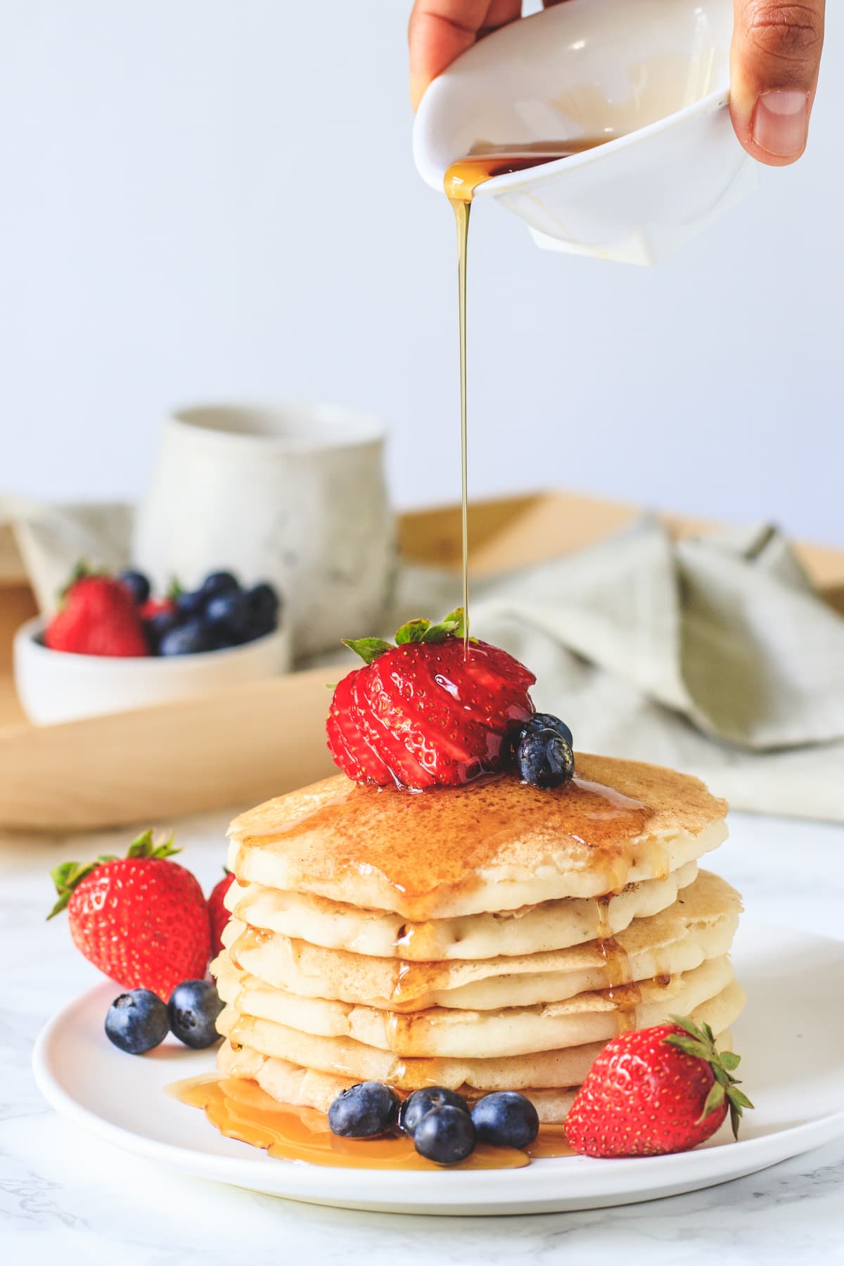 eggless panckes stacked in a plate with garnish of strawberries, blueberries and drizzle of maple syrup