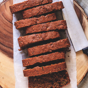 Eggless zucchini bread slices on parchment paper lined wooden tray with knife on side