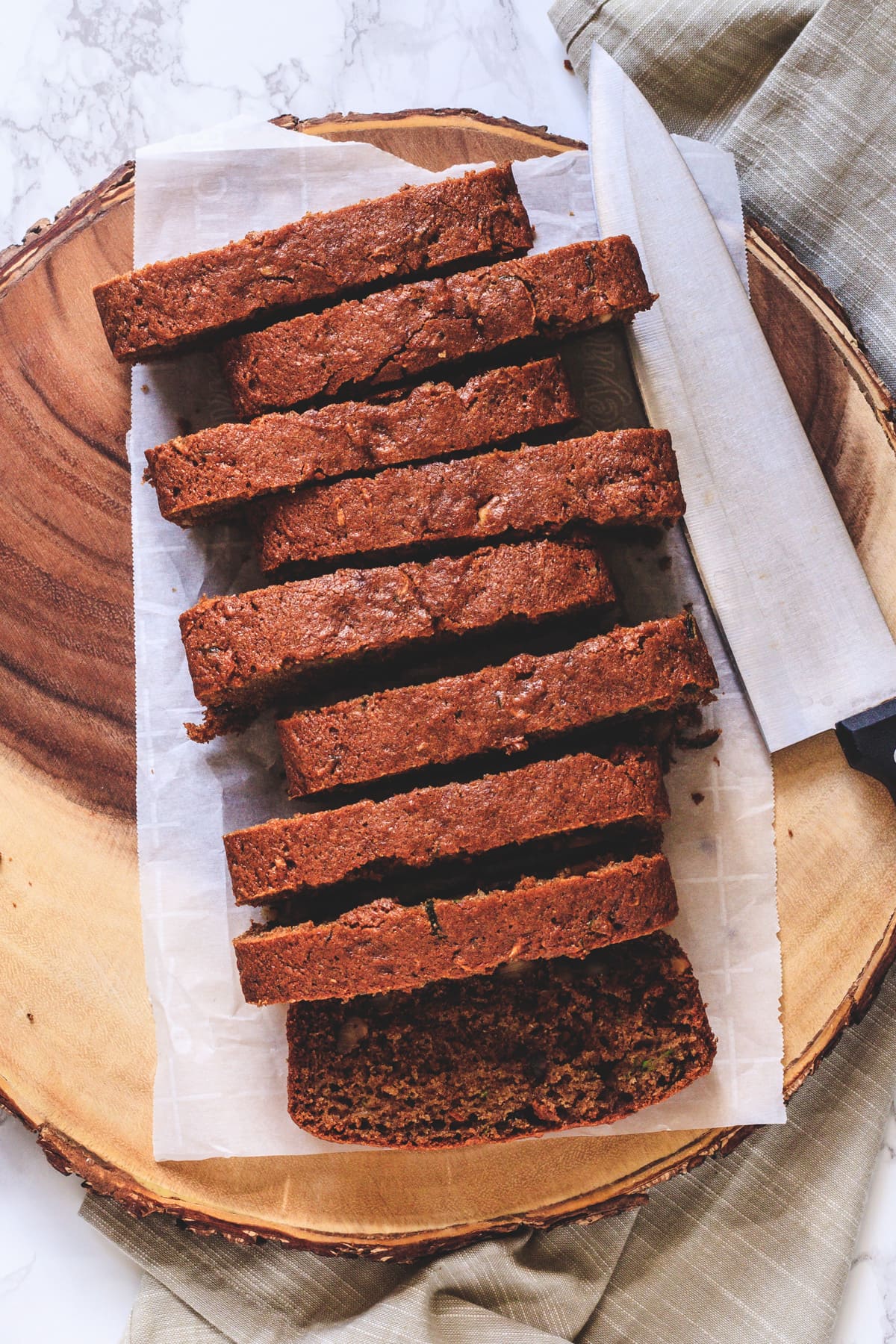 Eggless zucchini bread slices on parchment paper lined wooden tray with knife on side.