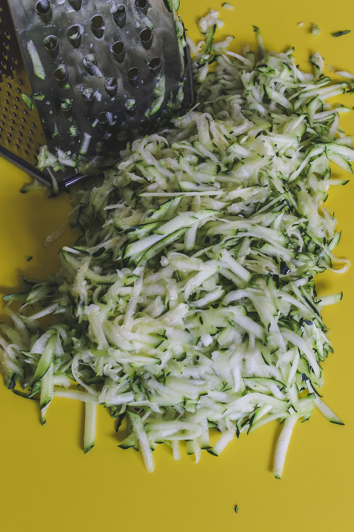 grated zucchini on yellow board with box grater on side