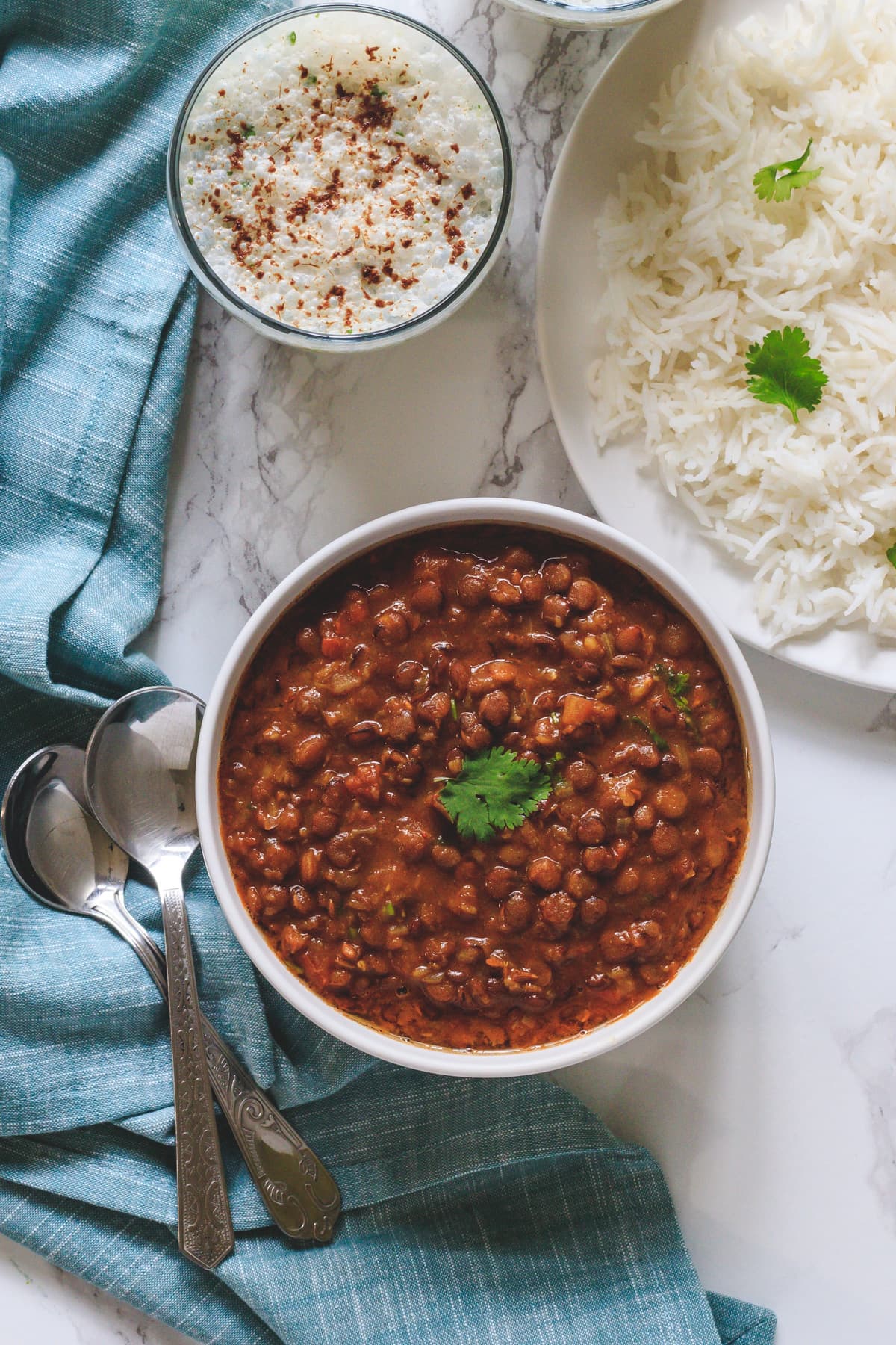 Lentil curry in a bowl with rice & buttermilk with napkin and spoons on side