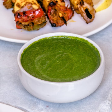 Mint chutney in a bowl served with paneer tikka on white marble slab