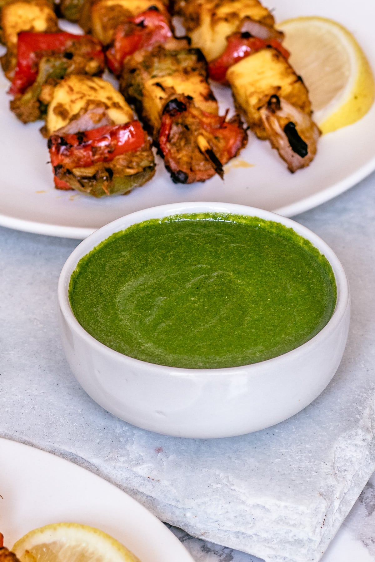 Mint chutney in a bowl served with paneer tikka on white marble slab