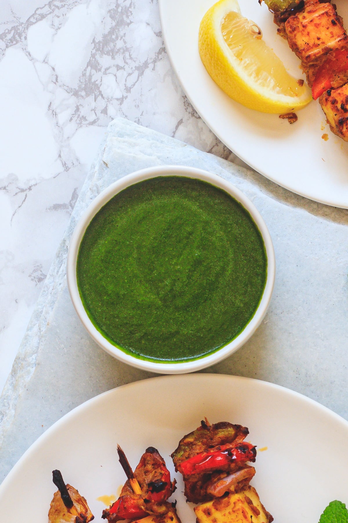 top view of mint chutney in a white with side of paneer tikka with lemon wedgebowl