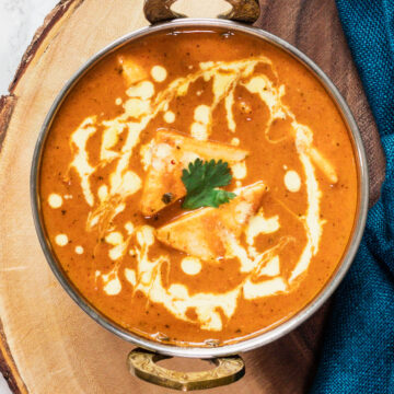 close up top view of shahi paneer in a serving wok on a wooden board