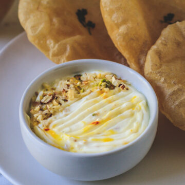 Shrikhand in a bowl with garnish of nuts served with pooris