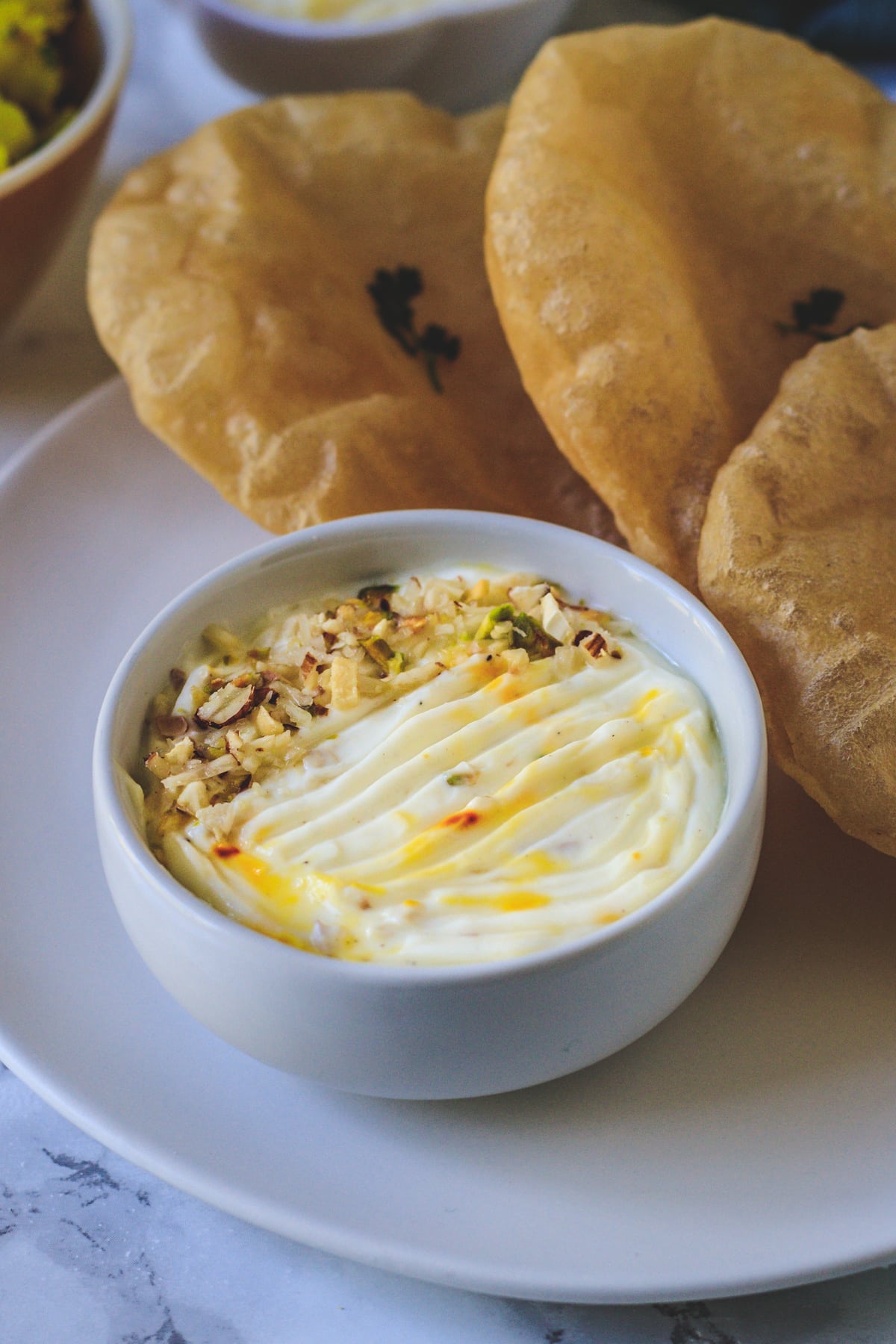 Shrikhand in a bowl with garnish of nuts served with pooris