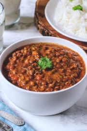 Close up of whole masoor dal in a white bowl with garnish of cilantro