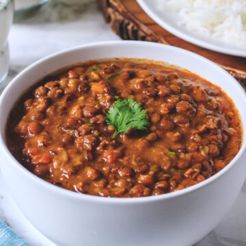 Close up of whole masoor dal in a white bowl with garnish of cilantro