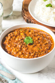 A bowl whole massor dal garnished with cilantro and rice in the back.