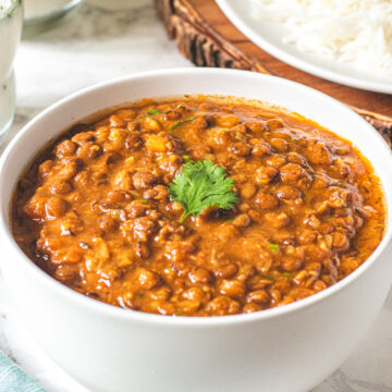 A bowl whole massor dal garnished with cilantro and rice in the back.