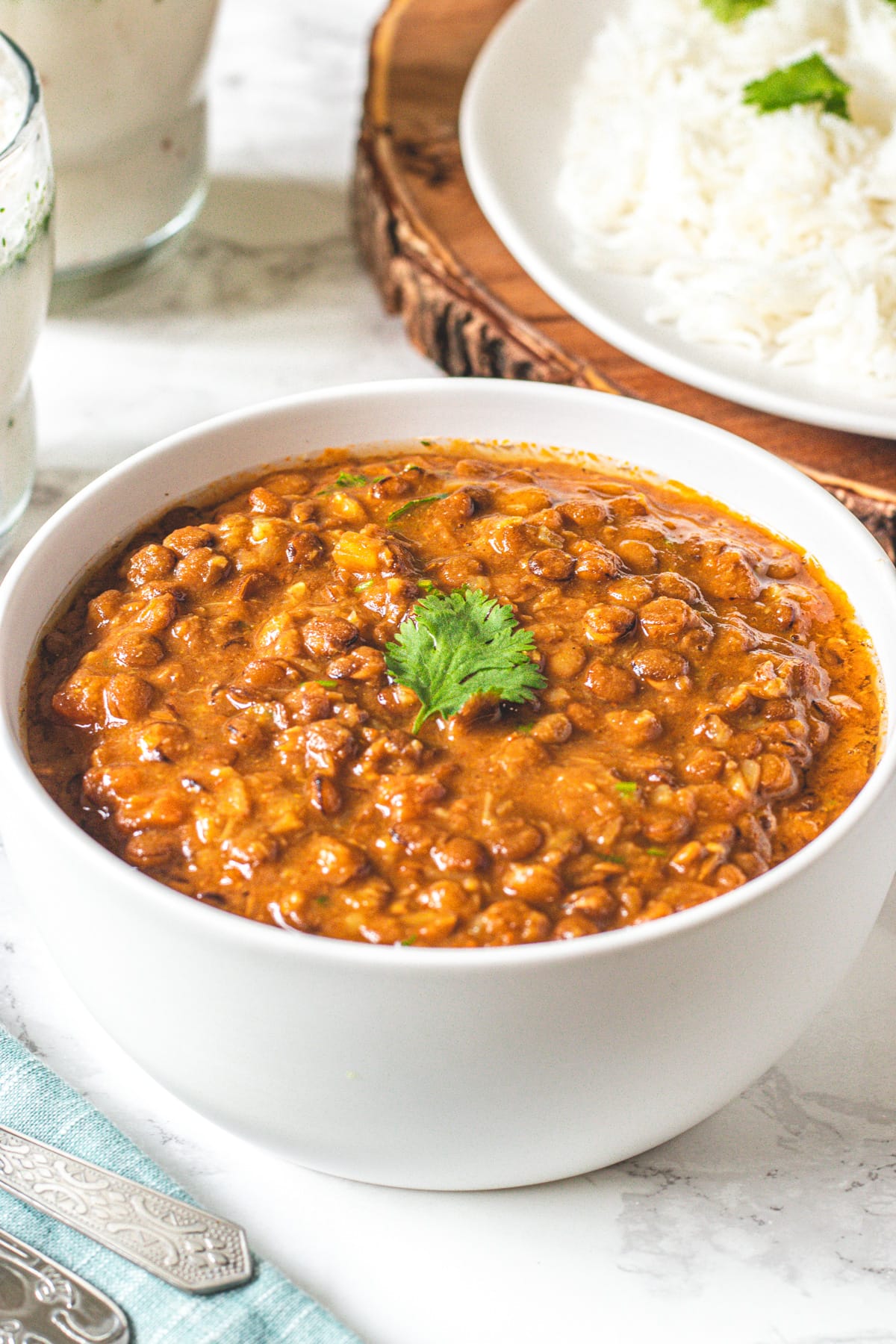 A bowl whole massor dal garnished with cilantro and rice in the back.