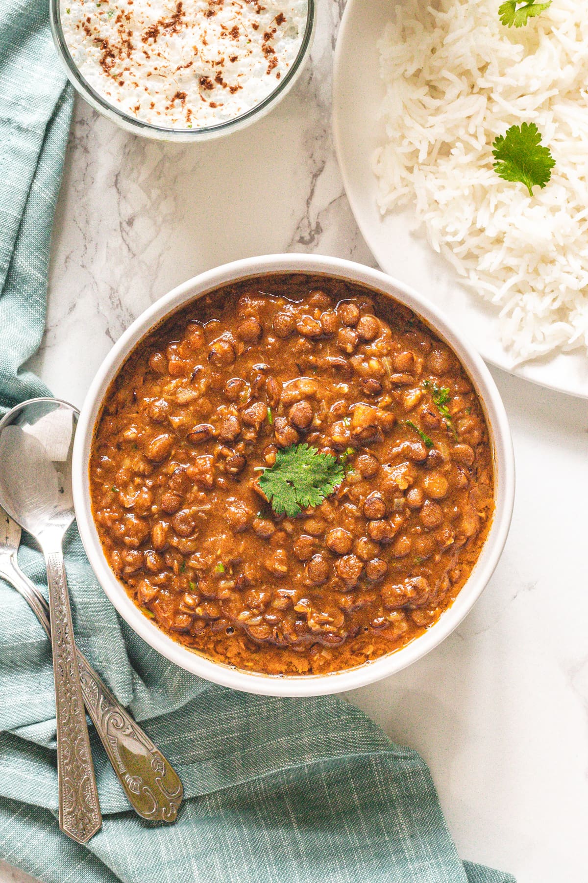 Whole masoor dal served with rice and chaas with spoons and napkin on the side.