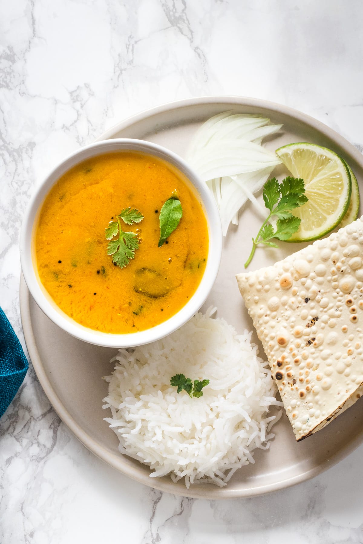 um prato com uma tigela de dal, arroz, papad, cebola fatiada e fatia de Limão Com Guarnição de folhas de coentros.