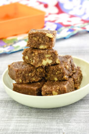 a stack of walnut burfi in a plate with orange container in the back ground