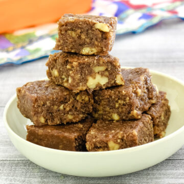 a stack of walnut burfi in a plate with orange container in the back ground