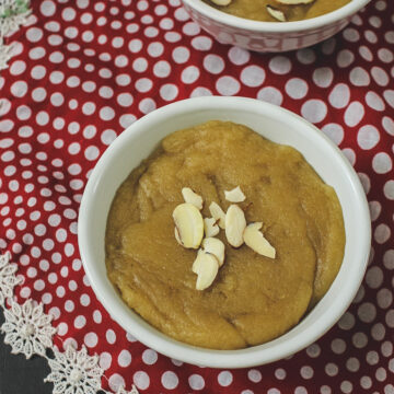 Wheat halwa in a bowl with garnish of almonds, another bowl in the back, polka dot napkin underneath