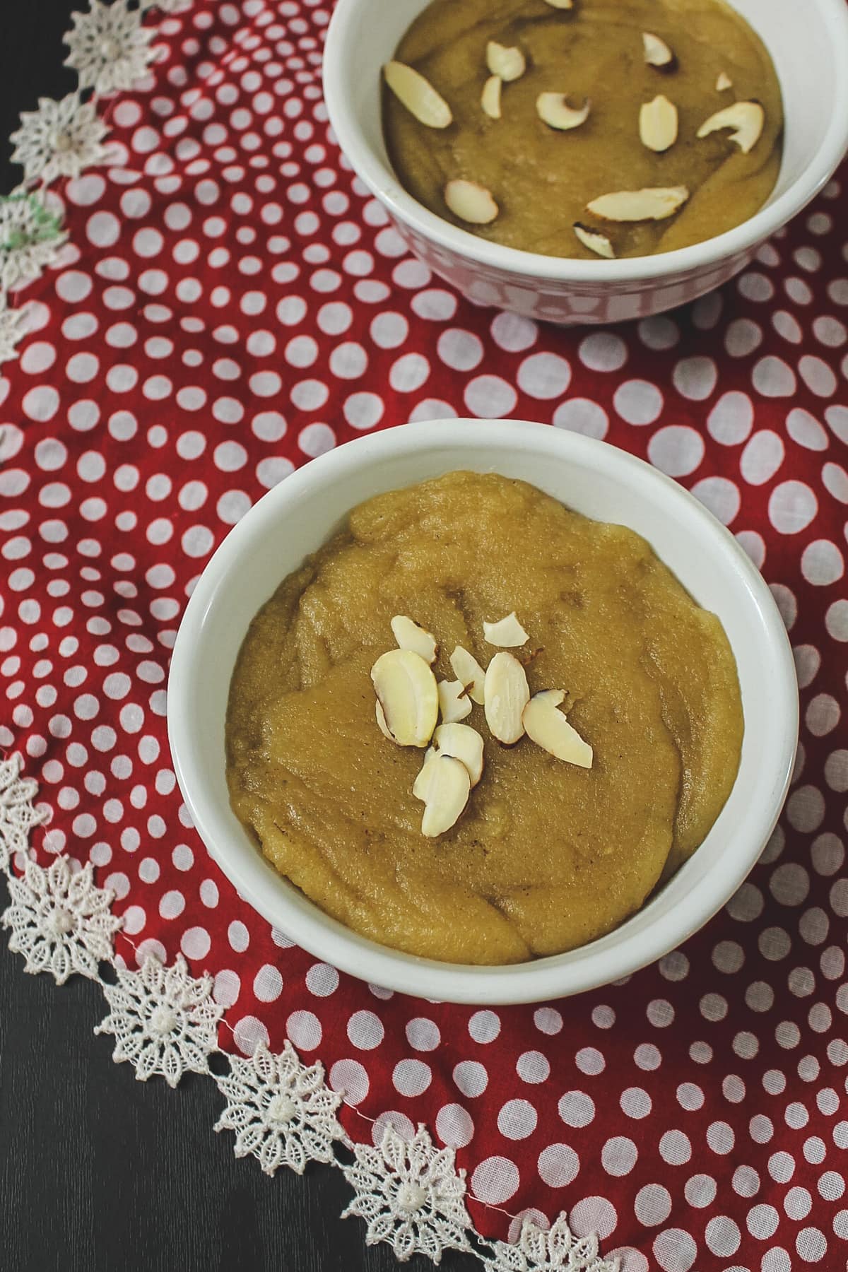 Wheat halwa in a bowl with garnish of almonds, another bowl in the back, polka dot napkin underneath