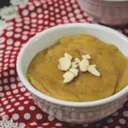 Close up image of atta halwa garnish with almonds in a white bowl with red decorative napking underneath