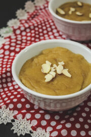 Close up image of atta halwa garnish with almonds in a white bowl with red decorative napking underneath