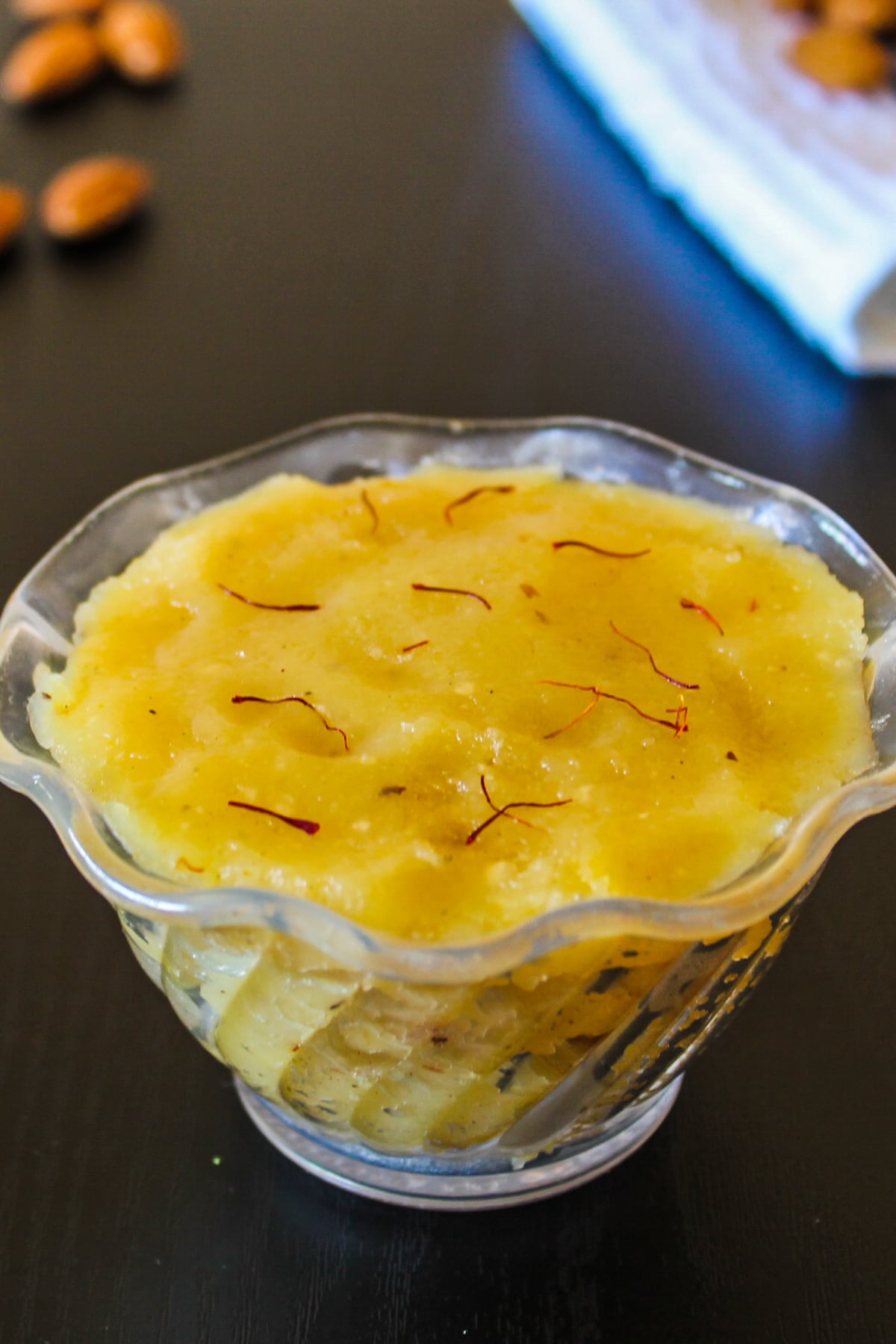 Badam halwa in a bowl garnished with saffron, few whole amonds are in the background