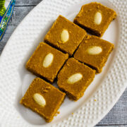 6 pieces of besan barfi in white oval plate with colorful napkin on side