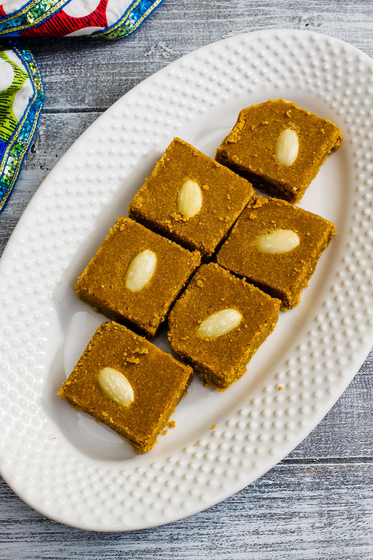 6 pieces of besan barfi in white oval plate with colorful napkin on side