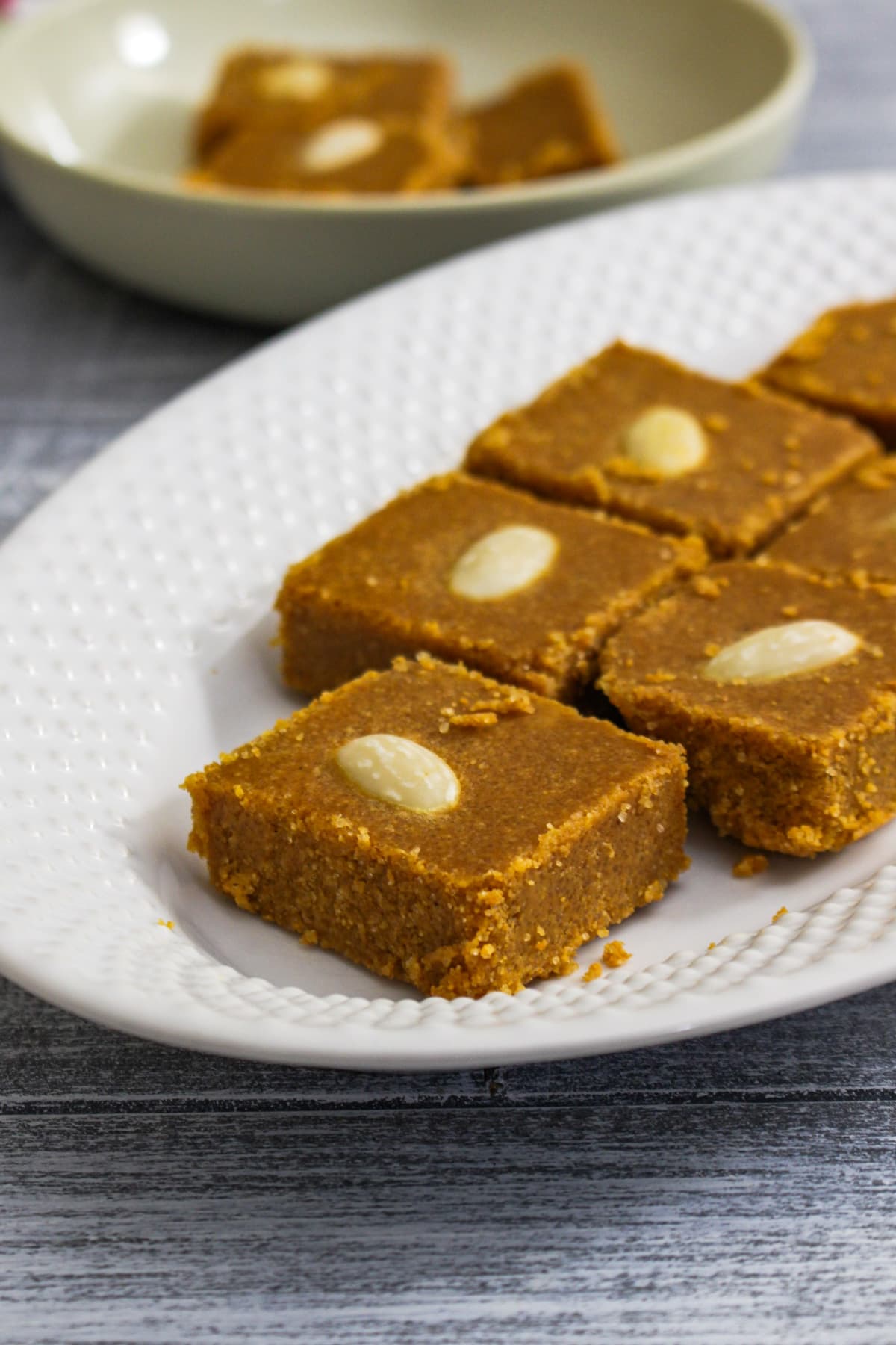 Close up of besan barfi garnished with sliced almond in white oval plate.