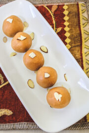 5 besan ladoo garnished with almonds arranged on rectangle plate with decorative napkin underneath