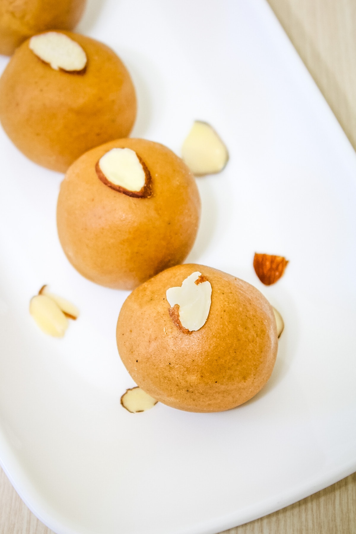 close up of besan ladoo garnished with slivered almonds in white plate