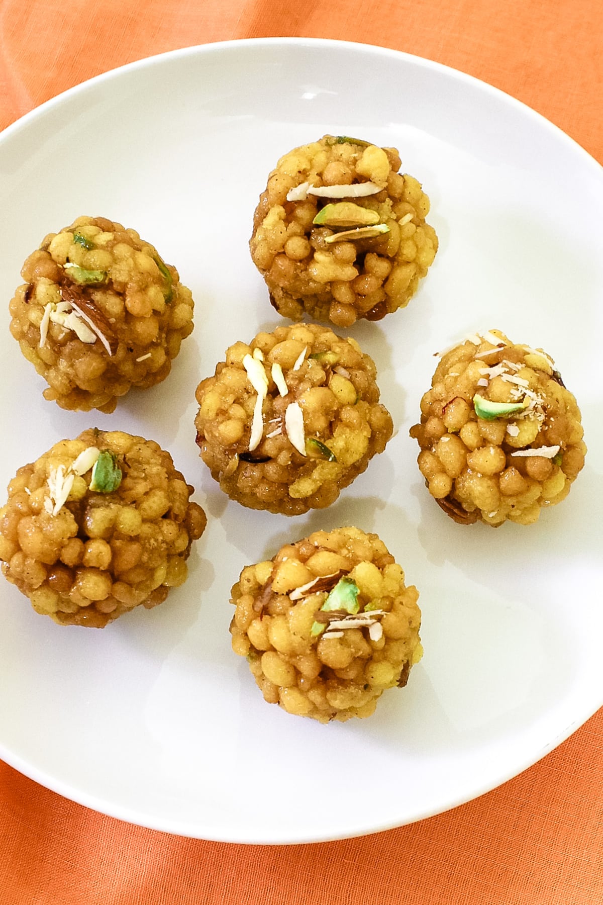 6 boondi ladoo with nuts garnish arranged on white plate with orange linen background