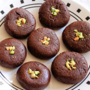 7 chocolate peda arranged on a plate with garnish of chopped pistachios