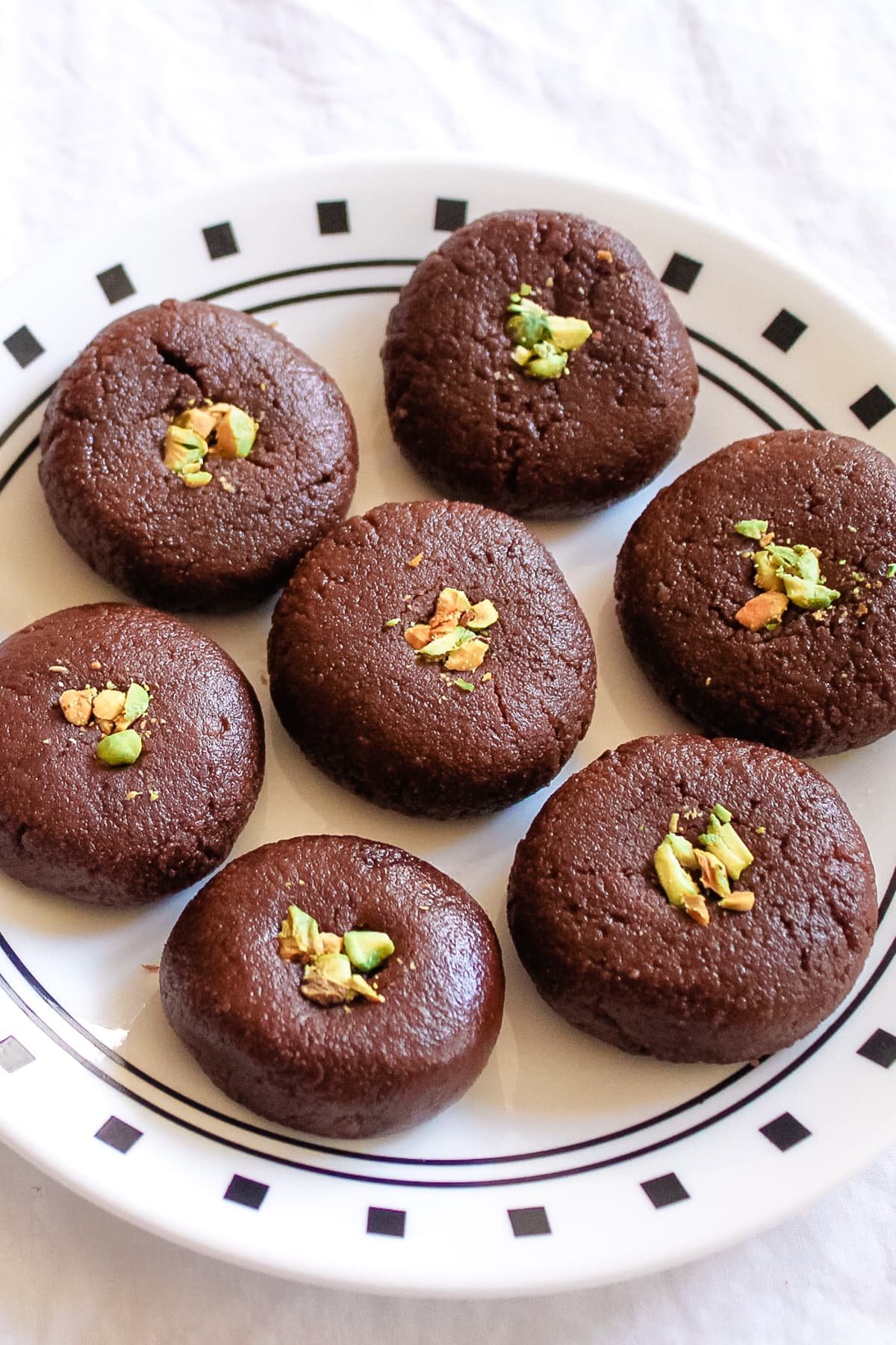 7 chocolate peda arranged on a plate with garnish of chopped pistachios