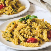 Corn pasta garnish with basil leaves in a white plate with another plate in the back with napkin