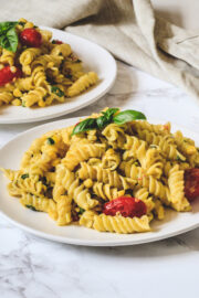 Corn pasta garnish with basil leaves in a white plate with another plate in the back with napkin